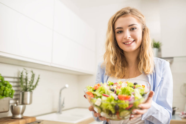 Young happy blonde girl preparing healthy salad in home kitchen - Photo, image