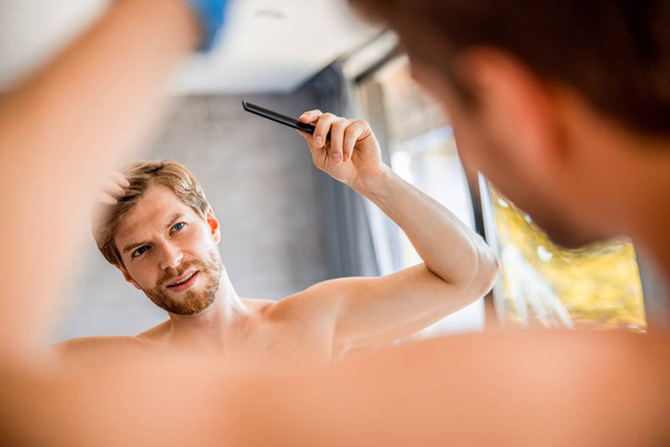 Улыбающийся молодой человек расчесывает волосы в ванной
 - Фото, изображение
