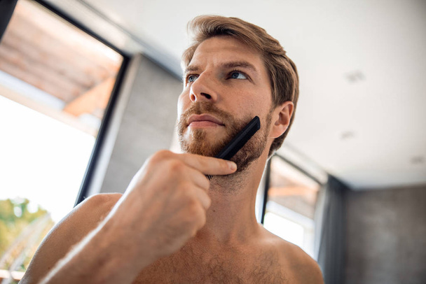 Attractive man brushing his beard in bathroom - Valokuva, kuva