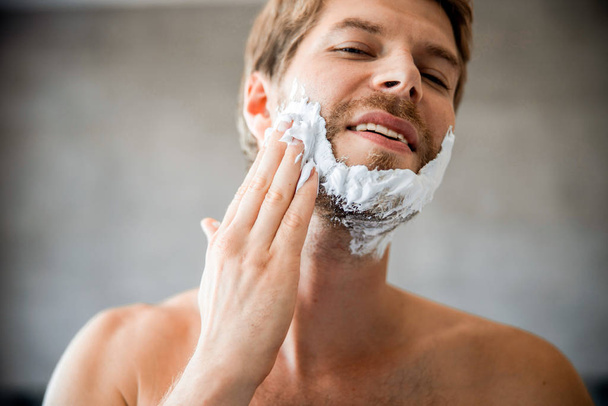 Joyful young man applying shaving cream on face - Fotoğraf, Görsel
