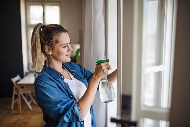Young woman standing indoors at home, cleaning windows. - Photo, Image