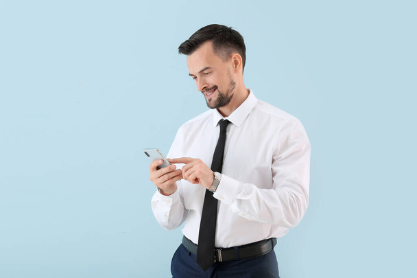 Portrait of young businessman with mobile phone on color background - Photo, Image