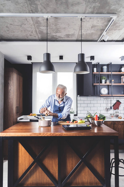 Picture of senior bearded handsome man standing at the kitchen cooking vegetables for lunch - Foto, imagen