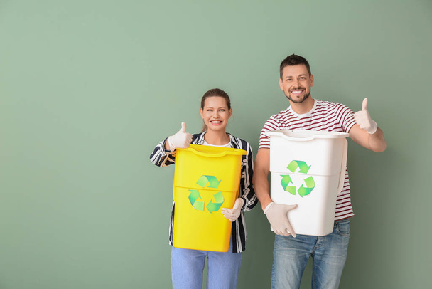 Ζευγάρι με δοχεία για σκουπίδια που δείχνουν τον αντίχειρα πάνω στο φόντο του χρώματος. Έννοια της ανακύκλωσης - Φωτογραφία, εικόνα