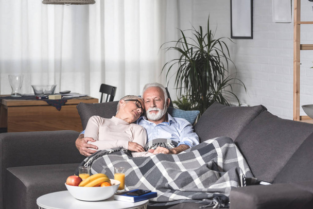 Senior husband and wife couple relaxing after lunch on sofa in living room covered with blanket. Relaxing time - Foto, immagini