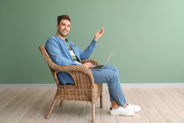 schöner Mann mit Laptop sitzt im Sessel in der Nähe der Farbwand - Foto, Bild