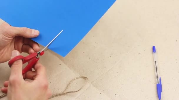 man tries to cut something out of blue paper with red scissors, make some craft work, but does not dare to do it, concept of indecision and hesitation or doubts, torment of creativity  - Video, Çekim