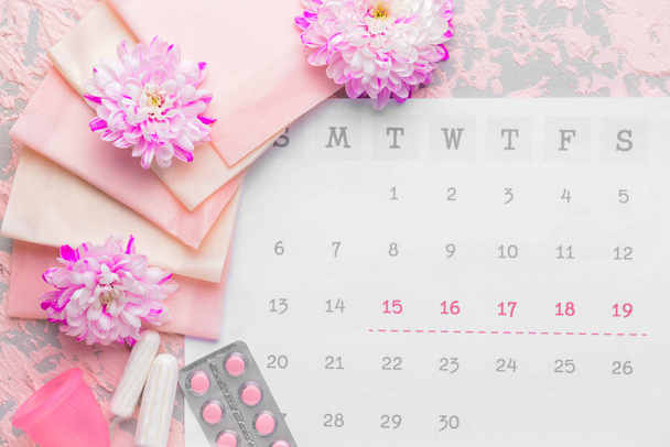 Menstrual calendar with feminine products and pills on color background - Foto, imagen