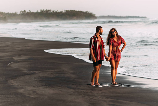 Happy couple holding hands walking on the sandy beach. Couple in love at sunset by the sea. Couple in love on vacation. Honeymoon trip. Romantic couple enjoying a beach walk at sunset - Foto, Imagem
