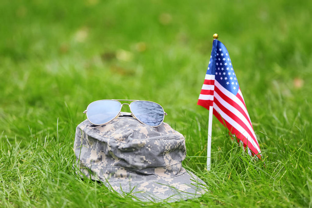 Military hat, sunglasses and USA flag outdoors. Memorial Day celebration - Photo, Image