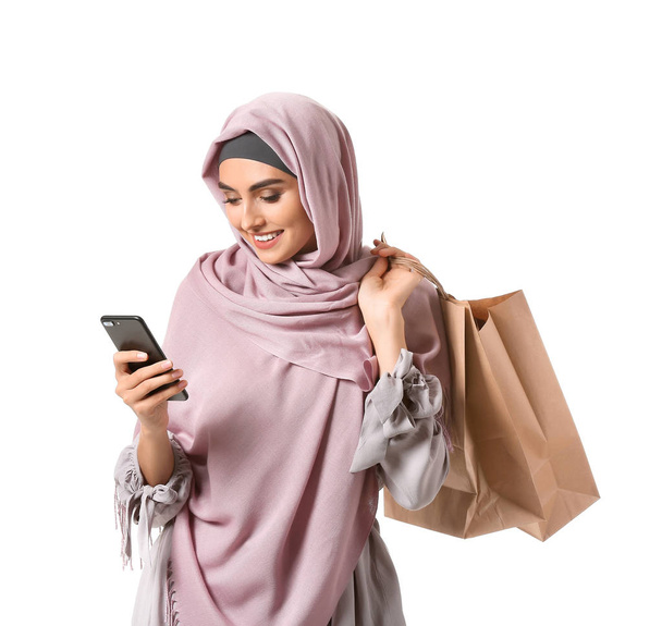 Hermosa mujer árabe con bolsas de compras y teléfono móvil sobre fondo blanco
 - Foto, Imagen