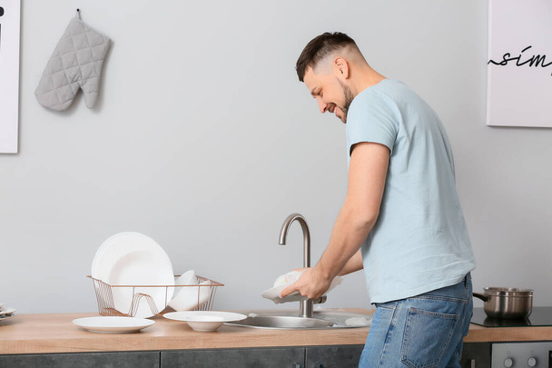 Handsome man washing dishes in kitchen - Foto, afbeelding