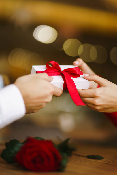 Man gives to his woman a gift box with red ribbon. Hands of man gives surprise gift box for girl. Lovers give each other gifts. Young loving couple celebrating Valentine's Day. Romantic day. - Foto, Imagen