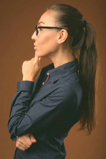 Jovem mulher de negócios bonita usando óculos contra fundo marrom
 - Foto, Imagem
