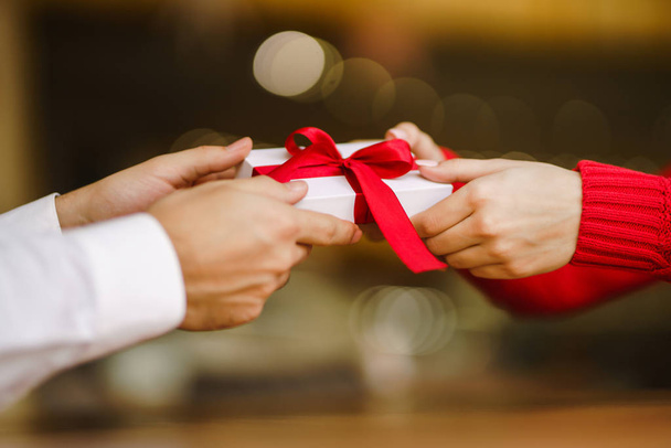Man gives to his woman a gift box with red ribbon. Hands of man gives surprise gift box for girl. Lovers give each other gifts. Young loving couple celebrating Valentine's Day. Romantic day. - Fotografie, Obrázek