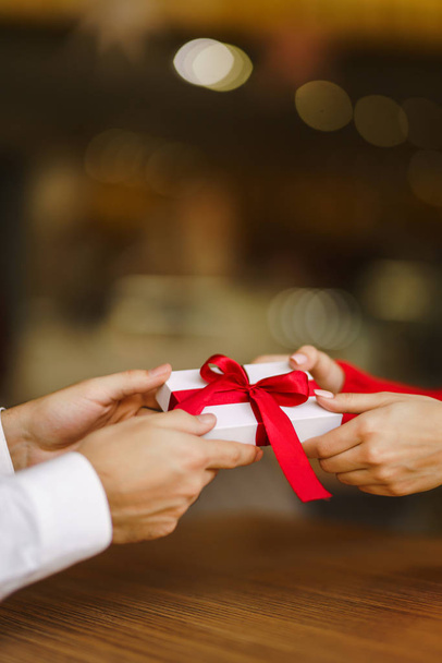 Man gives to his woman a gift box with red ribbon. Hands of man gives surprise gift box for girl. Lovers give each other gifts. Young loving couple celebrating Valentine's Day. Romantic day. - Photo, image