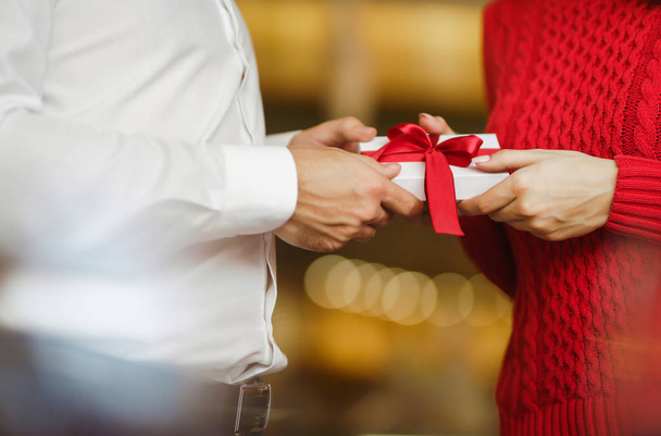 Man gives to his woman a gift box with red ribbon. Hands of man gives surprise gift box for girl. Lovers give each other gifts. Young loving couple celebrating Valentine's Day. Romantic day. - Photo, Image