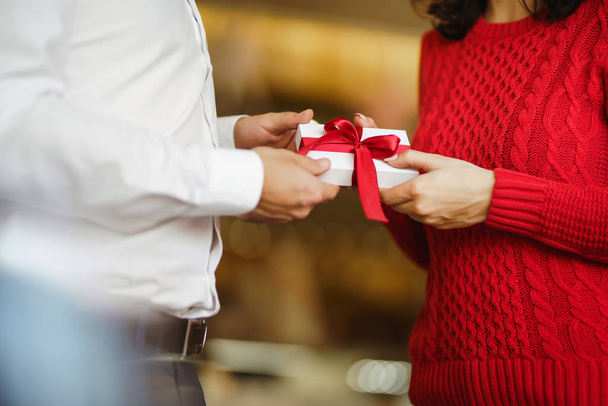 Man gives to his woman a gift box with red ribbon. Hands of man gives surprise gift box for girl. Lovers give each other gifts. Young loving couple celebrating Valentine's Day. Romantic day. - Photo, image