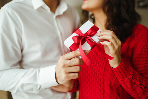 Valentine's Day, holiday and surprise concept. Man gives to his woman a gift box with red ribbon. A loving couple cuddles and celebrating Valentine's Day in the restaurant. Lovers give each other gift - Valokuva, kuva