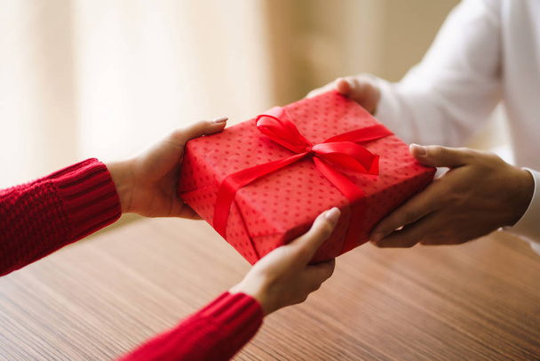 Valentine's Day, holiday and surprise concept. Man gives to his woman a red gift box. A loving couple celebrating Valentine's Day in the restaurant. Lovers give each other gifts. - Zdjęcie, obraz