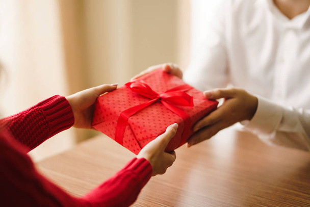 Valentine's Day, holiday and surprise concept. Man gives to his woman a red gift box. A loving couple celebrating Valentine's Day in the restaurant. Lovers give each other gifts. - Zdjęcie, obraz