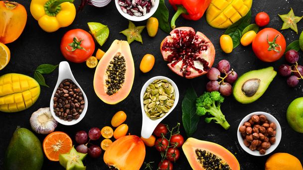 Organic food. Fruits, vegetables, beans and nuts on a black stone background. Top view. Free space for your text. - Foto, immagini
