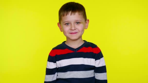 Porträt eines kleinen Jungen mit blauen Flecken im Gesicht, ein Kind posiert, schüchtern und lacht. gelber Hintergrund mit Kopierraum. Babygefühle. 4k Zeitlupe. - Filmmaterial, Video