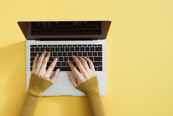 Tasainen lay kannettavan tietokoneen, kahvia ja kannettavan keltaisella pohjalla. Naisen kädet kirjoittaminen näppäimistöllä
 - Valokuva, kuva