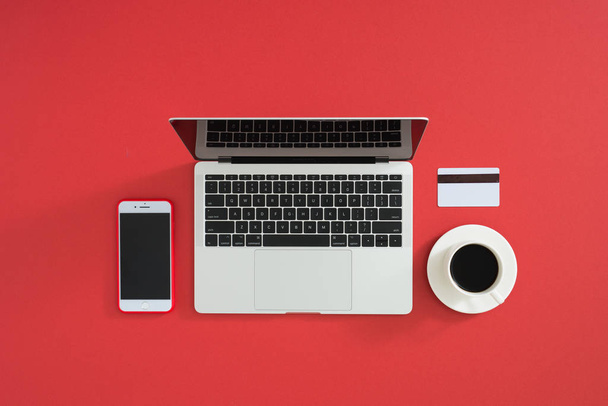 Płaskie zdjęcie obszaru roboczego z nowoczesnym laptopem, smartfonem, kawą i kartą kredytową, na tle koloru. - Zdjęcie, obraz