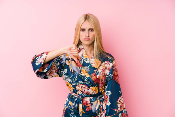 Young blonde woman wearing a kimono pajama showing a dislike gesture, thumbs down. Disagreement concept. - 写真・画像