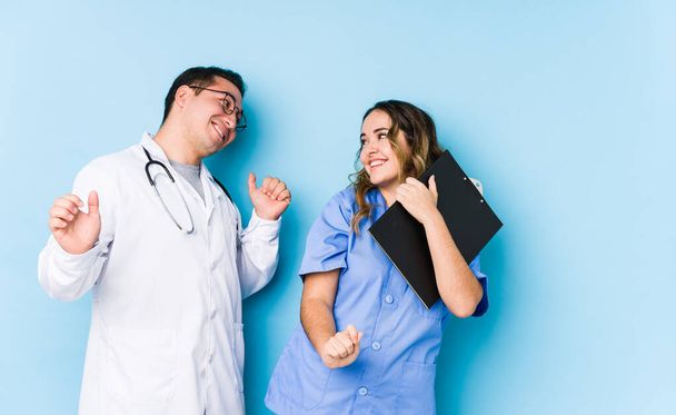Young doctor couple posing in a blue background isolated dancing and having fun. - Photo, image