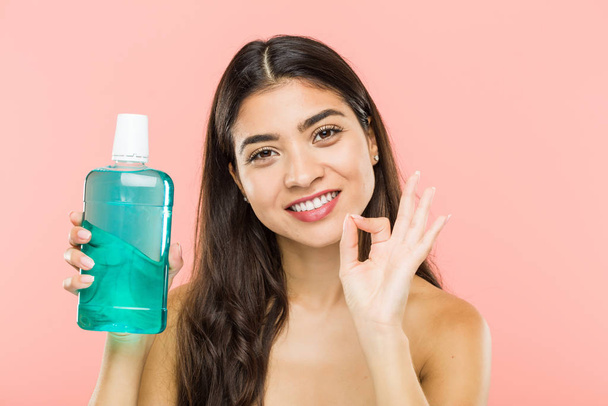 Young indian woman holding a mouthwash bottle cheerful and confident showing ok gesture. - Photo, Image