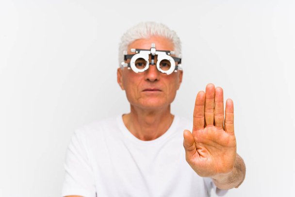 Homme caucasien senior portant un cadre de procès optométriste debout avec la main tendue montrant le signe d'arrêt, vous empêchant
. - Photo, image