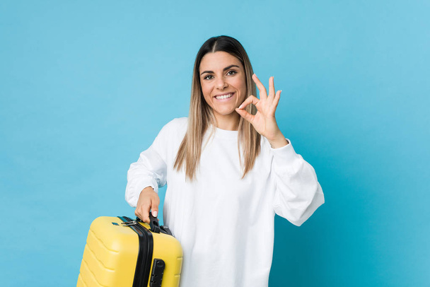 Young caucasian woman holding a suitcase cheerful and confident showing ok gesture. - Foto, Imagem