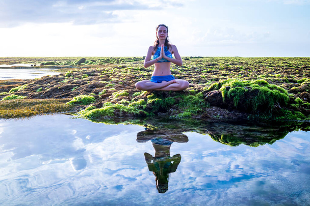 Jonge vrouw, mediterend, yoga beoefenend en pranayama op het strand. Sunrise yoga praktijk. Handen in de namaste mudra. Strand van Melasti, Bali - Foto, afbeelding