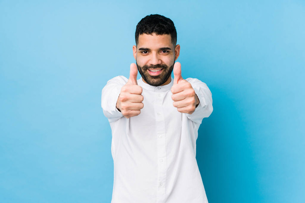 Young latin man against a blue  background isolated with thumbs ups, cheers about something, support and respect concept. - 写真・画像
