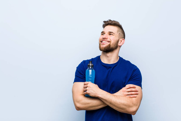Young caucasian sportsman holding an isotonic drink smiling confident with crossed arms. - Foto, immagini
