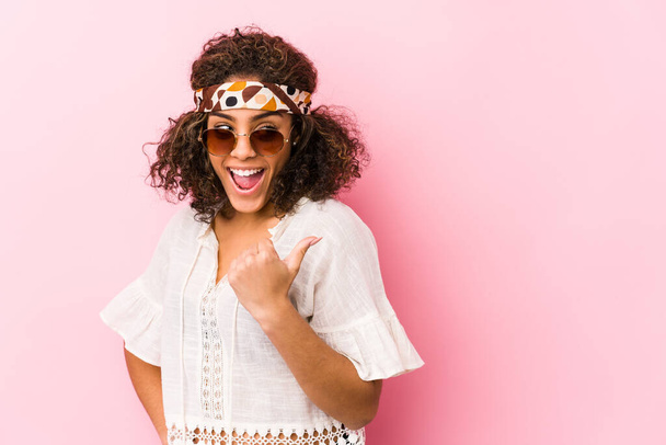 Joven mujer hipster afroamericana aislada en puntos de fondo rosa con el dedo pulgar lejos, riendo y sin preocupaciones
. - Foto, imagen