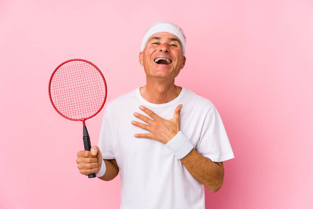 Middle aged man playing badminton isolated laughs out loudly keeping hand on chest. - Photo, Image