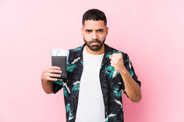 Young arabian cool man holding a boarding passes isolated showing fist to camera, aggressive facial expression. - Fotoğraf, Görsel