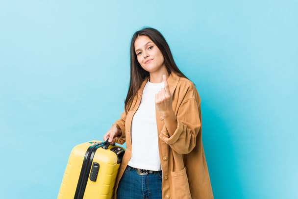 Young caucasian woman holding a suitcase pointing with finger at you as if inviting come closer. - Foto, Bild
