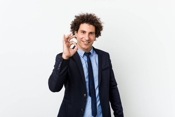 Молодой бизнесмен кудрявый человек на белом фоне веселый и уверенный в себе показывая ok жест
. - Фото, изображение