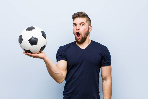 サッカーボールを持つ若い白人男性は、手のひらにコピースペースを保持して感銘を受けました. - 写真・画像