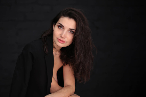 portrait of a beautiful young woman with dark hair in a black man's jacket on a dark background - Фото, изображение