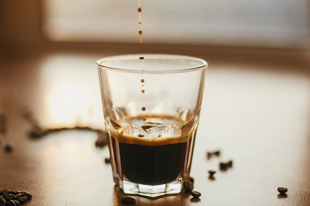 Капли кофе закрываются в теплом свете, наливая горячий эспрессо и
 - Фото, изображение