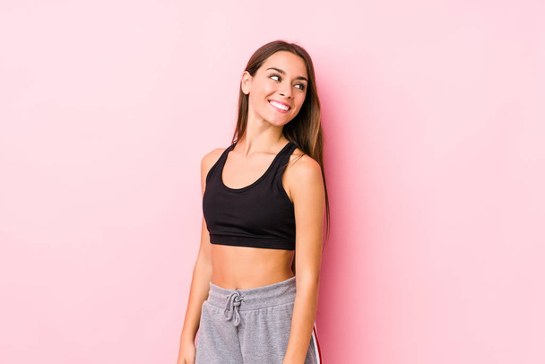 Joven caucásico fitness mujer posando en un fondo rosa se ve a un lado sonriente, alegre y agradable
. - Foto, imagen