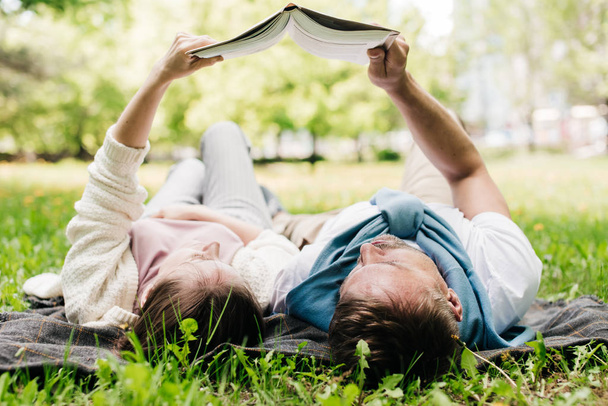 Ένα ζευγάρι ξεκουράζεται στο πάρκο διαβάζοντας ένα βιβλίο.. - Φωτογραφία, εικόνα