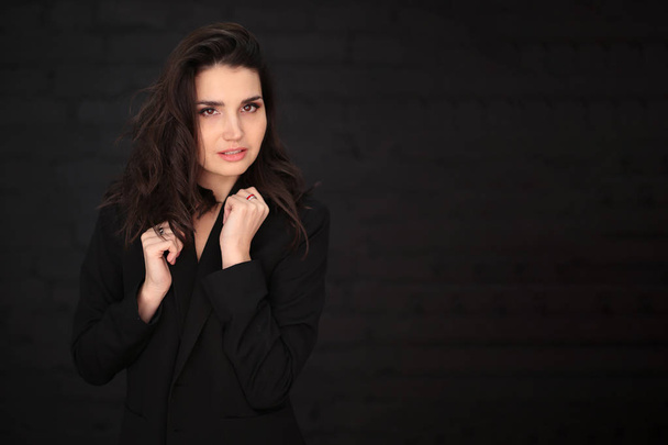 portrait of a beautiful young woman with dark hair in a black man's jacket on a dark background - Photo, Image