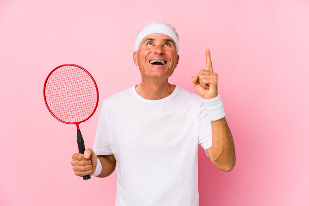 mężczyzna w średnim wieku gra badminton odizolowany wskazując do góry nogami z otwartymi ustami. - Zdjęcie, obraz