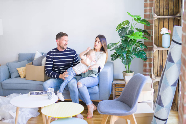 Bella famiglia con bambino seduto sul divano che tiene la lavagna in una nuova casa intorno a scatole di cartone
 - Foto, immagini